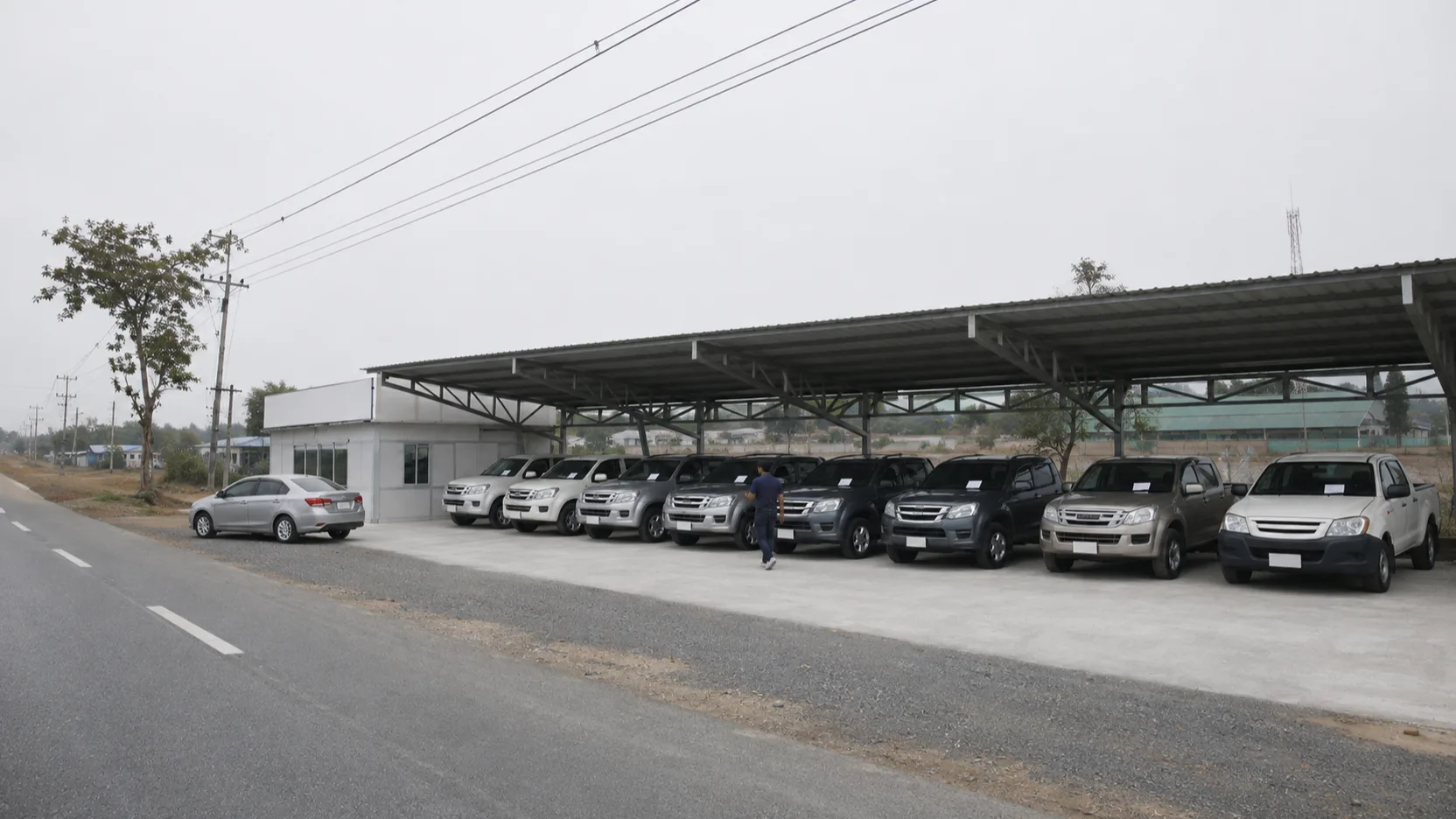 The lot seen from the Highway 1 frontage road — the steel canopy, the rows of pickups, the small office, a plain sign.