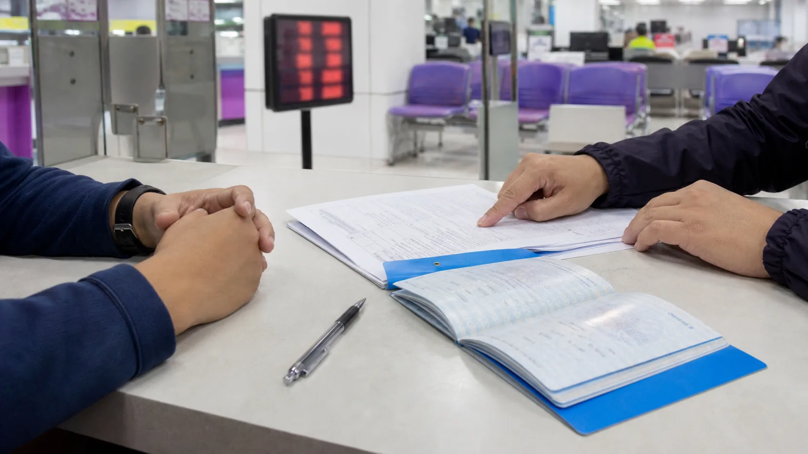 A registration book and transfer papers on a counter at the Land Transport Office, a customer and the transfer clerk on either side.